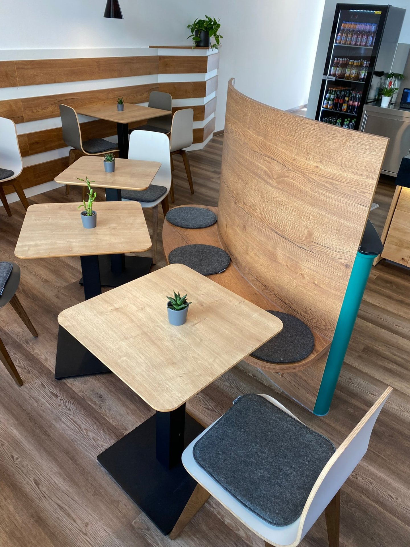 Bistrobereich mit geschwungener Holzbank, Tischen und Stühlen – Schreinerei Siegert
